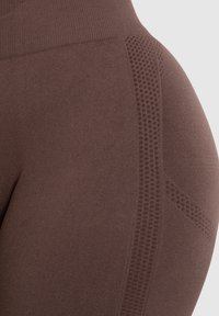 Bruine leggings met een gestructureerd patroon langs de zijkanten, met een hoge tailleband. Het materiaal lijkt rekbaar en glad te zijn.