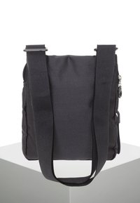 Svart budväska med texturerat tyg, justerbara remmar, ett överfång med dragkedja och sidofickor; kompakt rektangulär form.