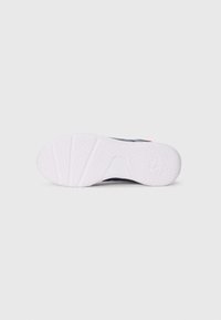 Semelle de chaussure de sport, avec un caoutchouc blanc texturé présentant des motifs hexagonaux, une section supérieure noire et des accents rouges près du talon.