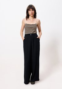 Zwarte brede pijpenbroek met een hoge taille en twee zijzakken, gecombineerd met een zwart-wit gestreepte tanktop.