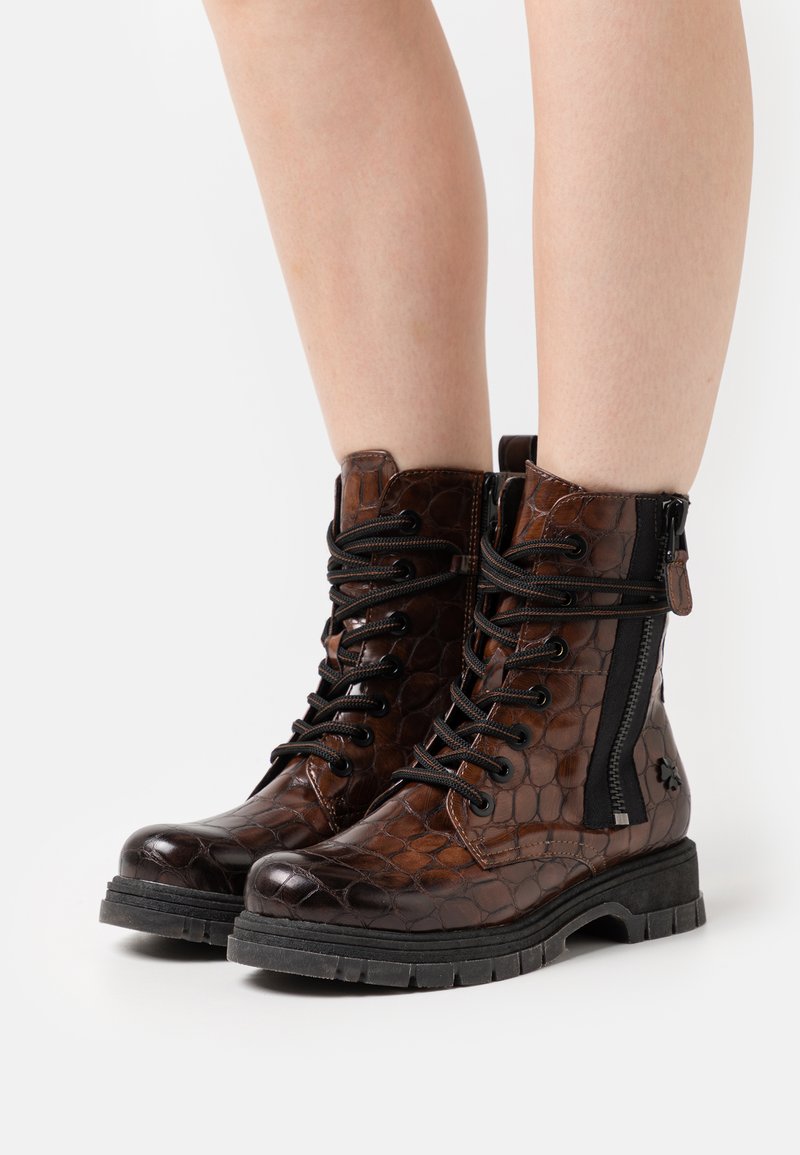 Bottines en cuir marron avec un motif texturé ressemblant à du crocodile, détail de fermeture éclair noire, bout rond et semelle en caoutchouc robuste.
