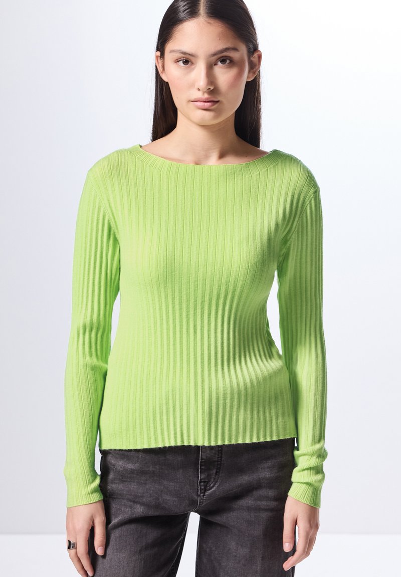Maglione a maniche lunghe a costine di un vivace verde lime, con scollo ampio e silhouette aderente, abbinato a jeans grigio scuro.