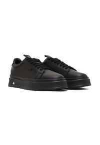 Sneakers neri con tomaia in morbida pelle, punta arrotondata, lacci neri piatti e suola in gomma spessa e testurizzata. Accento triangolare notevole sul tallone.