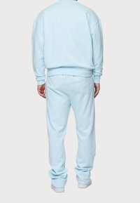 Sudadera de algodón azul claro y pantalones de chándal, con un corte relajado, puños y cinturilla de punto. Textura suave sin patrones visibles.