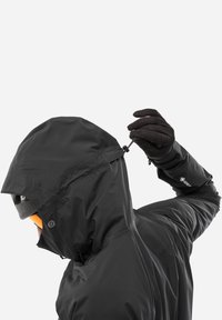 Veste noire imperméable avec une capuche ajustée, un cordon de serrage réglable et un col intérieur doux. Le tissu semble lisse avec une finition mate.