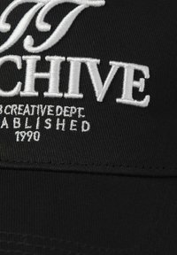 Black cap featuring white embroidered text. Includes "ARCHIVE" and smaller text detailing creative department and the year 1990.