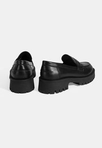 Zwarte leren instappers met een chunky zwarte rubbersole met een robuuste textuur, een slip-on ontwerp en gelaagde stikselaccenten.