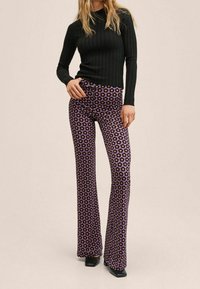 Czarna prążkowana bluzka z długim rękawem w połączeniu z fioletowymi spodniami w kształcie dzwonów z kwiatowym wzorem. Spodnie mają gładką fakturę i dopasowany fason w talii.