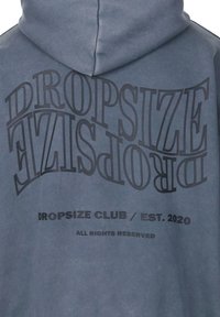 Kapuzensweatshirt aus gedämpftem blauen Stoff mit auffälligem schwarzen Text, darunter "DROPSIZE CLUB / GEGRÜNDET 2020" und stilisiertem "DROPSIZE."