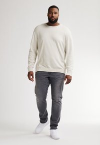 Maglione a maniche lunghe color beige chiaro, texture morbida, collo a giro; abbinato a jeans slim-fit grigio scuro e sneakers bianche. Design semplice e moderno.