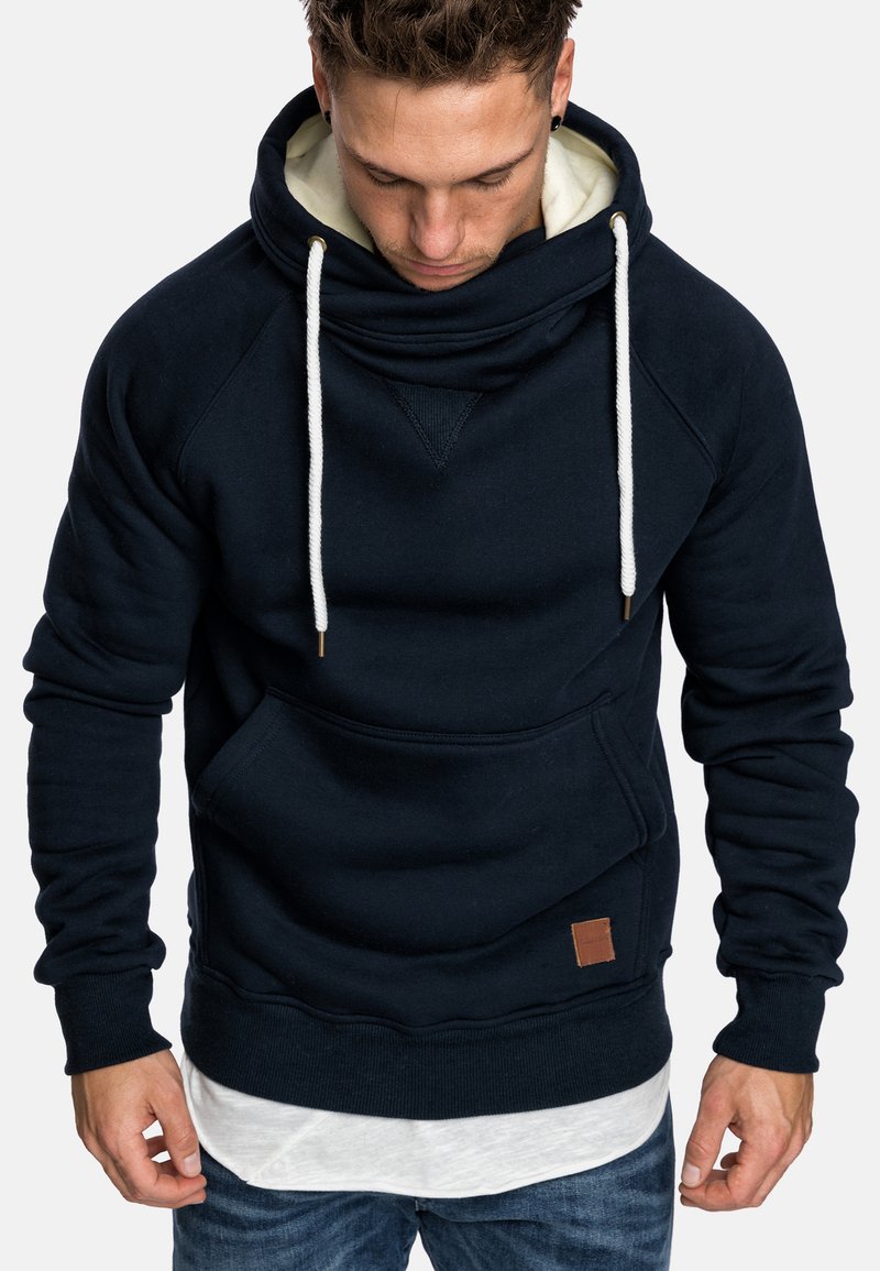 Navy blue hoodie with a high collar and drawstrings, featuring a front pocket and leather tag detail. Made of soft, textured fabric.
