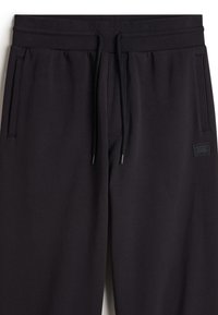 Schwarze Sweatpants aus weichem Material mit elastischem Bund und verstellbarem Kordelzug. Mit Seitentaschen und einem Vans-Logo-Patch.