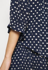 Marinblå klänning med krämfärgade prickar, som har puffärmar, en avslappnad passform och plisserad textur vid fållen.
