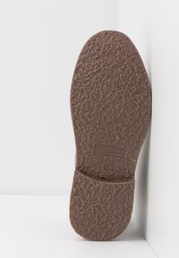 Hnědá gumová podešev s texturovaným povrchem; obsahuje embosované jméno značky "JACK & JONES" a výrobní detaily.