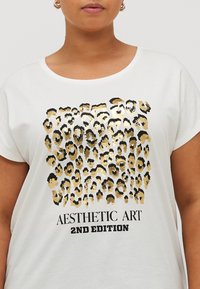 White short-sleeve t-shirt featuring a gold and black leopard print design and bold text stating "AESTHETIC ART 2ND EDITION."