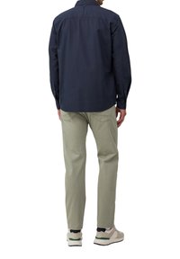 Marineblauwe overhem shirt met lange mouwen en achterkant met detail, gecombineerd met lichtgroene broek en grijze sneakers met zwarte en groene accenten.