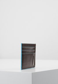 Cartera de cuero marrón con bordes azules, que cuenta con varios compartimentos para tarjetas y un acento metálico. Textura lisa y diseño minimalista.
