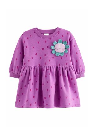 Lilla bomulds kjole med lange ærmer, der har en indsnævret talje, lyserøde prikker og en blomsterformet stoflap på brystet.