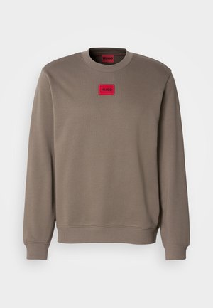 Brun bomullssweater med rund hals. Har en rektangulær rød logomerke på brystet. Ribbestrikkede ermer og kantene for tekstur.