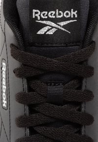 Gros plan sur la languette et les lacets d'une chaussure noire Reebok, montrant le logo blanc Reebok brodé sur la languette et l'étiquette latérale.