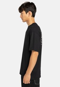Zwarte katoenen t-shirt met korte mouwen, ronde halslijn en grafisch detail op de achterkant. Kenmerkt zich door een relaxte pasvorm en een zachte textuur.