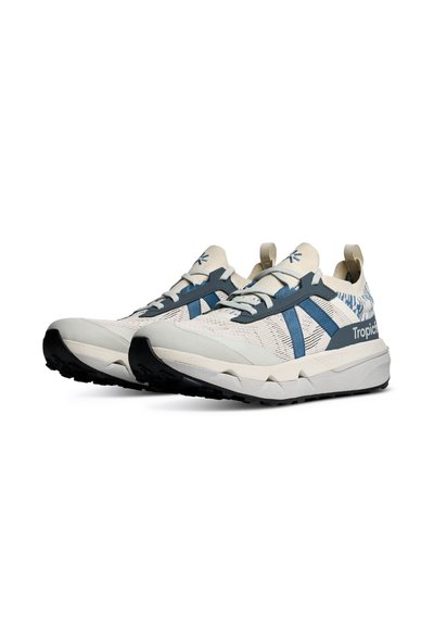 Paire de baskets basses blanches avec des rayures bleues, semelles texturées et languettes sur fond blanc.