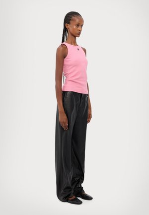 Top rosa senza maniche, slim fit, con logo ricamato; abbinato a pantaloni in pelle nera a vestibilità ampia e scarpe nere flat.