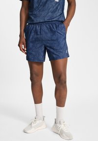 Marina atletiska shorts i lätt material, med en randig mönster, elastisk midja och sidfickor, kombinerat med ljusa sneakers.