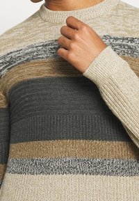 Gebreide trui met horizontale strepen in beige, bruin, grijs en zwart. Geribde halslijn en manchetten, textuurstof met verschillende steekpatronen.