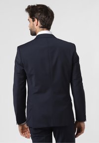 Navy suit with structured shoulders, tailored fit, single-vent back, and detailed stitching. White dress shirt collar visible.