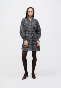 Button-up dress in dark gray with a repeated pattern, belted waist, balloon sleeves, and a flared skirt, paired with dark tights and heels.