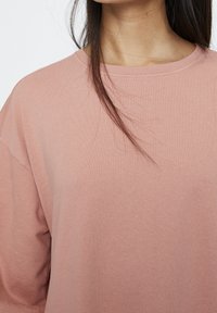 Hellrosa Pullover mit lockerer Passform, geripptem Kragen, weichem Material und überschnittenen Schultern, der glattes Gewebe und dezente Nähte präsentiert.