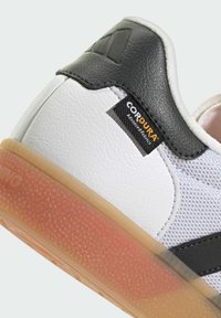 White sneaker with a textured leather black overlay, mesh panels, and a semi-transparent orange rubber sole. Features a CORDURA label.