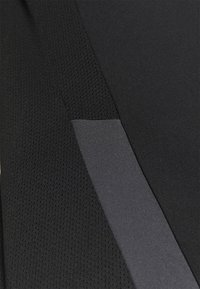 Tissu sportif noir avec une section en maille texturée et une bande lisse et unie. L'accent varie en teinte, offrant un contraste visuel.