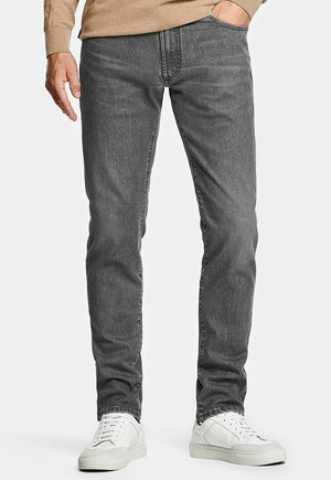 Jean en denim gris avec une coupe slim, poches standard et détails de délavage subtils, associés à des baskets blanches et un pull beige clair.