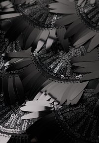 Tissu noir orné de sequins en forme de pétale brillants et de sequins circulaires disposés en motif tourbillonnant, avec une finition texturée.