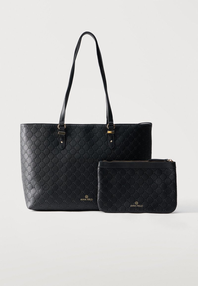 Sac fourre-tout noir et pochette zippée assortie avec motif embossé et marquage doré "Anna Field" sur un fond blanc uni.