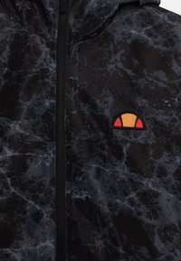 Kurtka w czarno-marmurkowanym wzorze z zamkiem błyskawicznym, z małym, kolorowym haftowanym logo na klatce piersiowej. Gładki, lekki materiał.
