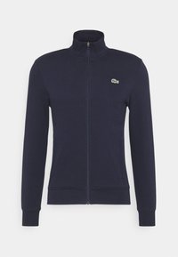 Giacca zip-up blu navy con maniche lunghe, colletto alto e piccolo logo di coccodrillo verde sul lato sinistro del petto.