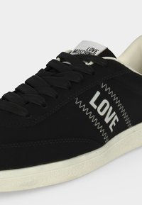 Baskets noires avec semelle blanche, lacets noirs, et "LOVE" brodé sur le côté, avec "LOVE MOSCHINO" sur l’étiquette de la languette.