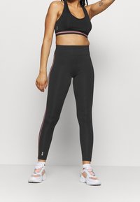 Svart sportbehå med en rosa rand i botten, kombinerad med svarta leggings med rosa sidorandar. Outfiten har en figurnära design och en slät textur.