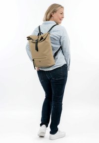 Taschenrolltop-Rucksack in Tan mit schwarzen Riemen, einer Front-Reißverschlusstasche und strapazierfähigem Material. Das Design weist eine schlanke, minimalistische Form auf.