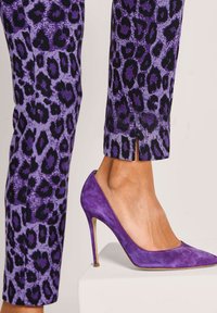 Paarse luipaardprintbroek met een kleine proportie-spleet, gecombineerd met paarse suède hoge hakken met een spitse neus op een witte blok.