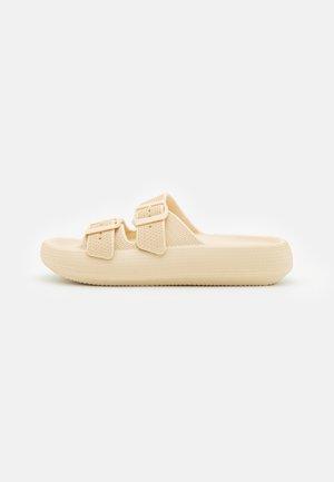 Beige Slidesandale mit profilierter Sohle und zwei verstellbaren Schnallenriemen, Seitenansicht vor weißem Hintergrund.