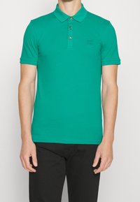 Polo vert en coton, doté d'un col classique, d'un plastron à trois boutons et d'un logo discret sur la poitrine.