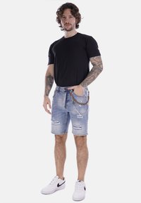 Shorts de mezclilla en azul claro, con detalles rasgados, un accesorio de cadena y una camiseta negra ajustada, combinados con zapatillas blancas.