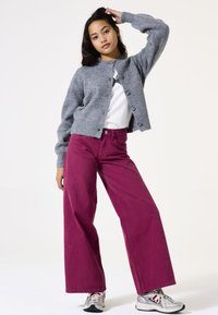 Cárdigan de punto acanalado gris con cuello redondo, detalles de botones, combinado con pantalones de pierna ancha fucsias y zapatillas deportivas plateadas.