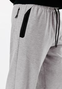 Grå sweatpants med struktureret stof, elastisk talje og sorte lynlåslommer til opbevaring.