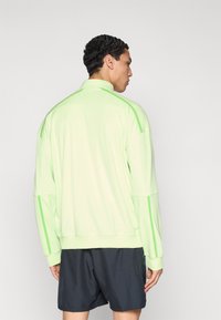 Ανοιχτοπράσινο πουλόβερ με ψηλό γιακά, μακριά μανίκια και σκούρο γκρι σορτς σε αντίθεση. Λεία υφή και μινιμαλιστικός σχεδιασμός.