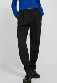 Zwarte op maat gemaakte broek met plooien, voorzien van een rechte pijp, verstelbare koordjes bij de enkels en een gladde stoftextuur.